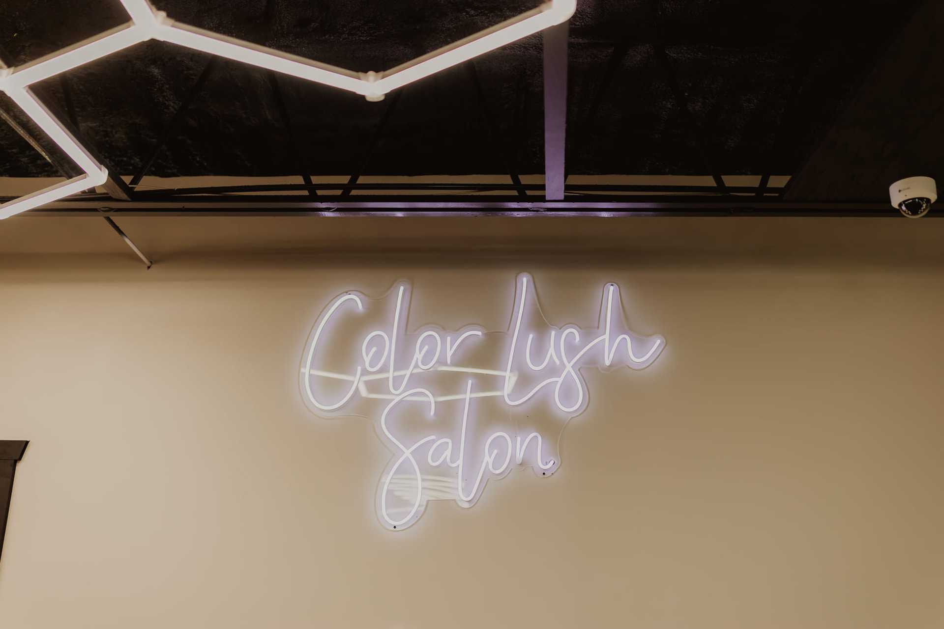 Neon sign reading "Color Lush Salon" on a beige wall.